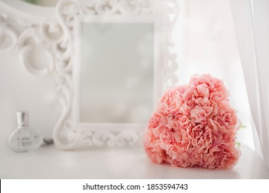 Pink flowers on the dressing table in the white bedroom. Flowers and perfumes in a bright interior. White boudoir table close up and copy space.
