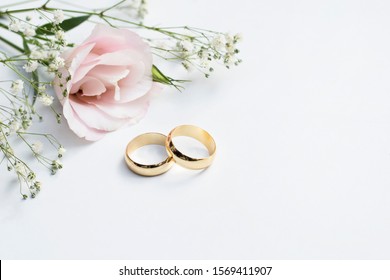 Pink flowers and two golden wedding rings on white background. - Shutterstock ID 1569411907