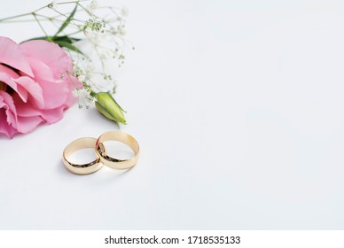 Pink flowers and two golden wedding rings on white background.	