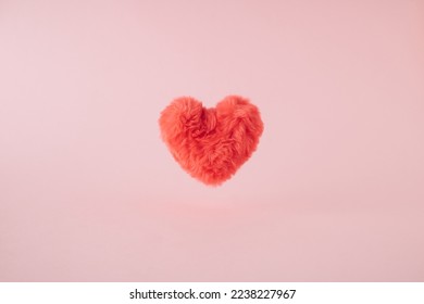 Pink fluffy plush heart levitating above pastel background.