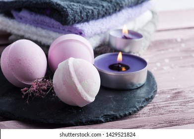 Pink foaming bath bombs on stone plate, spa concept with towels and lit aroma candles