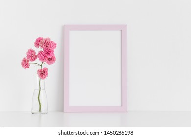 rosafarbene Rahmen mit rosafarbenen Rosen in einer Glasvase auf einem weißen Tisch zusammengesteckt.Porträtausrichtung.