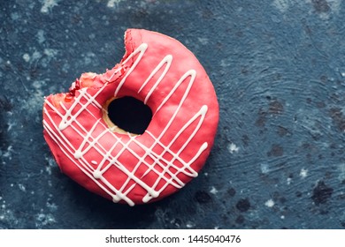 Pink frosted donut with bite missing on dark background. Top view. Copy space.