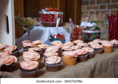 Pink frosted vanilla and chocolate cupcakes sit on a table cloth of burlap with other candies in the background as a dessert table for a wedding.