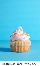 Pink frosted vanilla cupcakes with sprinkles on a bright blue background