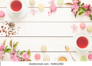 Pink Fruity Tea And Pastel French Macarons Cakes On Rustic White Wooden Background. Dessert In A Garden. Flat Lay Composition (from Above, Top View). Free Text Space.