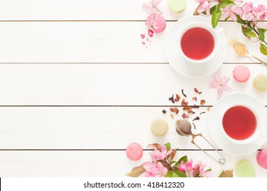 Pink Fruity Tea And Pastel French Macarons Cakes On Rustic White Wooden Background. Dessert In A Garden. Flat Lay Composition (from Above, Top View). Free Text Space.