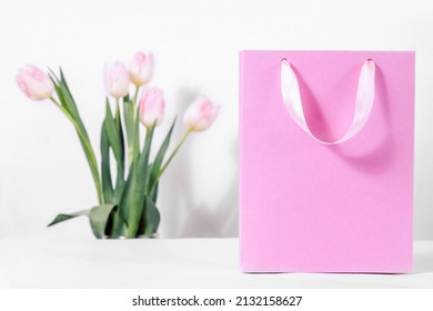 A pink gift bag with delicate tulip flowers on a white background. Discounts and sales for the spring women's holiday on the eighth of March - Powered by Shutterstock