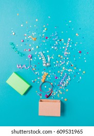 Pink Gift Box With Various Party Confetti, Streamers, Noisemakers And Decoration On A Blue Background. Colorful Celebration Concept.