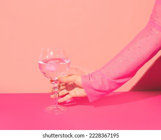 Pink gin cocktail in a highball glass and female hand against bright wall. Girls party idea. 