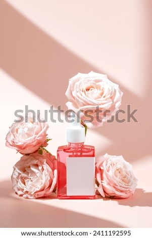 Pink glass cosmetic bottle with a dropper on pink background with rose flowers and hard shadows. Natural cosmetics concept, natural essential oil and skin care products, mockup