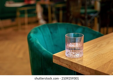 A Pink Glass Of Water On The Edge Of A Wooden Table At The Cafe, A Green Chair 