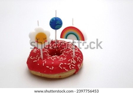 Pink glazed strawberry donut with springles and spring flower rainbow and earth day ecology space traveling on top snack and dessert foods served on white background