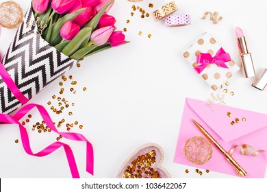 Pink and Gold Styled Desk with Florals. Pink tulips in black and white stylish wrapping paper, gifts, cosmetics and female accessories with confetti on white background