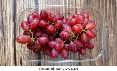 Pink Grapes In A Plastic Container Stand On A Brown Wooden Table.view From Above. Grona Grapes