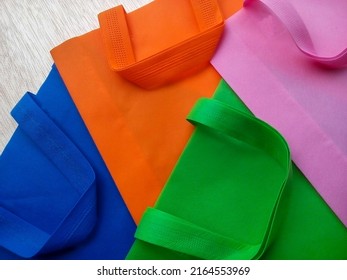 pink, green, orange and blue polypropylene bags. a pile of tote bags made of non-woven fabric with folds on a white fibrous board
