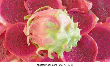 Pink And Green Whole Dragonfruit On Top Of A Texture Of Layered Dragon Fruit Slices, Top View Shot. Creative Footage Of A Delicious Exotic Tropical Fruit. Bright Harvest Of Asian Farms.