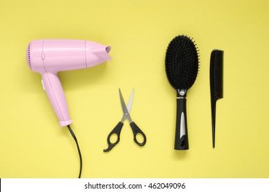 Pink hair dryer black brush, comb and scissors on yellow paper background