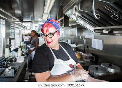 Pink haired chef puts on work gloves aboard busy food truck - Powered by Shutterstock