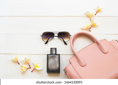 Pink Hand Bag ,sunglasses And Black Bottle Perfume Accessories Of Lifestyle Woman Relax Summer With Flower Frangipani Arrangement Flat Lay Style On Background White Wooden