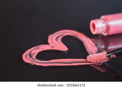 Pink heart drawn by lipgloss and open lip gloss bottle isolated on black mirror surface background with reflection