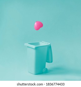 Pink heart falling in garbage bean against pastel blue background. Broken, fake, lost love. Minimal relationship concept.
