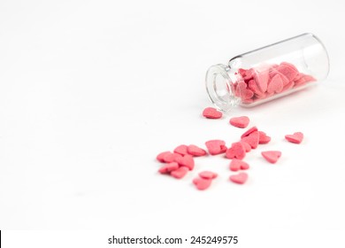 Pink heart-shaped sugar sprinkles fall out from a tiny glass, isolated on a white background.