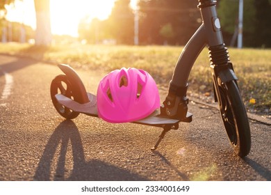 A pink helmet lies on a children's scooter against the backdrop of a sunset in the summer. The concept of safety while riding a scooter. - Powered by Shutterstock