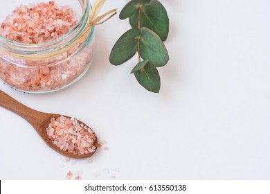 Pink Himalayan salt in glass jar, green eucalyptus branch, wooden spoon on white background, top view, spa, wellness, health concept