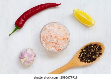 Pink Himalayan salt on the glass bowl, red hot chili pepper, piece of lemon, fresh garlic and mix of peppers in a wooden spoon on the white background. Top view copy space. Set of various spices. - Powered by Shutterstock