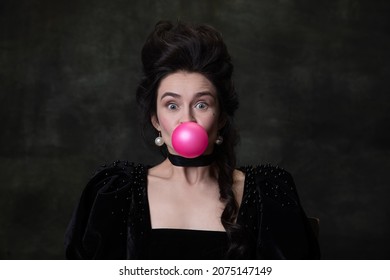 Pink and huge bubble. Close-up portrait of young pretty woman in image of medieval royal person having fun isolated on dark background. Concept of funny meme emotions, modernity and renaissance.