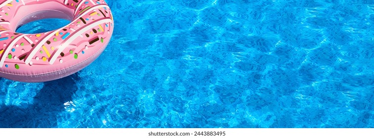 Pink inflatable donut with sprinkles floats in blue swimming pool. Water in pool is clear and there are few small waves on surface. Ring is floating on water, and its reflection can be seen in pool. - Powered by Shutterstock