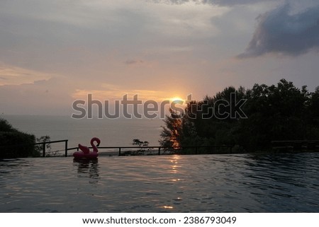 Pink inflatable flamingo floating in swimming pool water.  Sunset sky view.