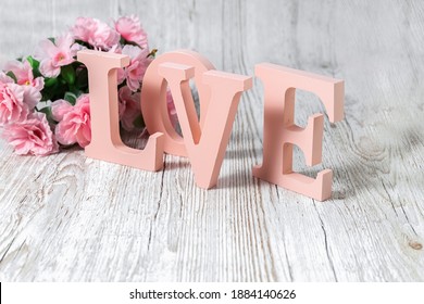 Pink letters and flowers on a wooden background. The word Love. Wooden volumetric letters. Valentine's Day. Wedding props.