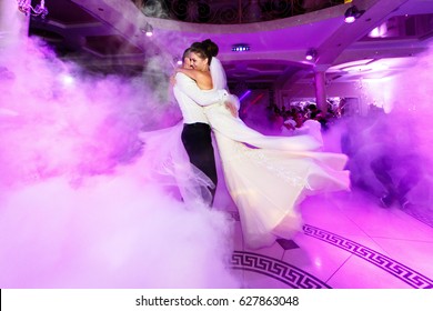Pink light illuminates wedding couple dancing in the smoke