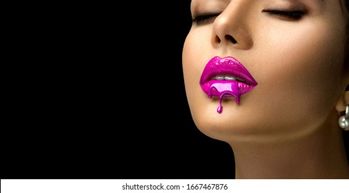Pink Lipstick dripping. Paint drops on red lips, lipgloss dripping from sexy lips, Purple liquid drops on beautiful model girl's mouth, creative abstract make-up. Beauty woman face makeup close up