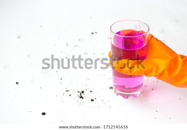 Pink liquid in a glass cup, hand in a protective glove holds a glass