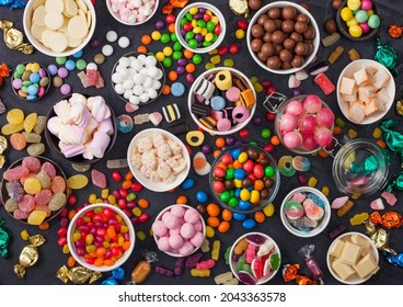 Pink lollipop candies in jar with various milk chocolate and jelly gums candies on black with liquorice allsorts and strawberry bonbons and large variety of sweets and candies. - Shutterstock ID 2043363578