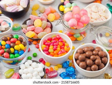 Pink lollipop candies in jar with various milk chocolate and jelly gums candies on white with liquorice allsorts and strawberry bonbons