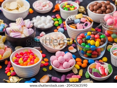 Pink lollipop candies in jar with various milk chocolate and jelly gums candies on black with liquorice allsorts and strawberry bonbons and large variety of sweets and candies.