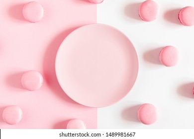 Pink macaroons, empty pink plate on pink and white background. Sweet background. Flat lay, top view, copy space