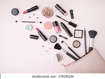 A pink makeup bag with cosmetic beauty products spilling out on to a pastel colored background, with empty space at side - Shutterstock ID 570190234