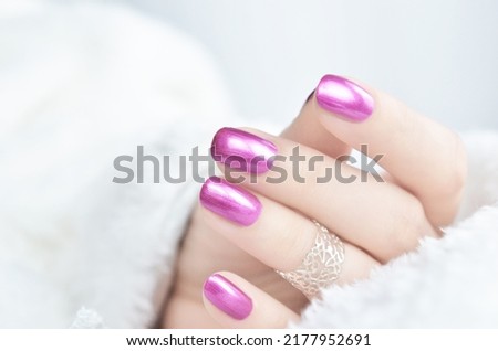 Pink metallic manicured nails on white fur.