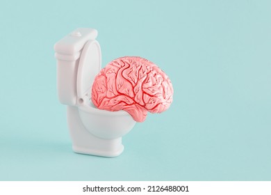 Pink model of human brain sitting on the white toilet on isolated pastel blue-green color background. Minimal abstract surreal concept of different ideas, brainstorming, brainwashing or brain fog.