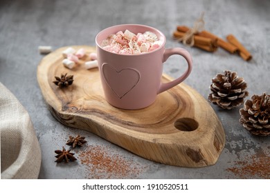 Pink mug with flavored cocoa and white-pink marshmallows, cinnamon sticks, star anise, on a wooden board. Close up - Powered by Shutterstock