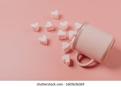 a pink mug lies on its side against a pink background, light-pink marshmallows sprinkled from it in the form of hearts - Shutterstock ID 1603636369