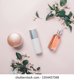 Pink natural cosmetics: oil, serum, cream, mask on background with flowers. Flat lay, minimalism.