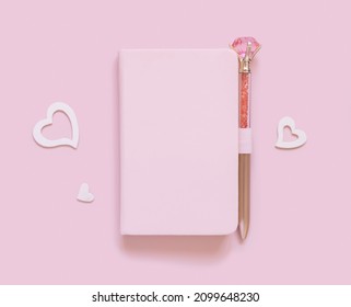 Pink notebook, decorative gemstone pen and hearts on light pink top view. Minimal scene with textbook mockup. Planner cover with place fot text. Valentines, educational and girly concept