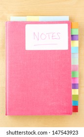 Pink notebook on a light wood background.  White 'Notes' label on cover, three tab dividers along top edge and fifteen down right side.  Eighteen tabs in total, left blank to provide space for text.