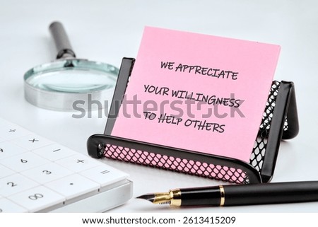 A pink notepad featuring an encouraging message sits on a black desk organizer alongside a calculator and a pen.